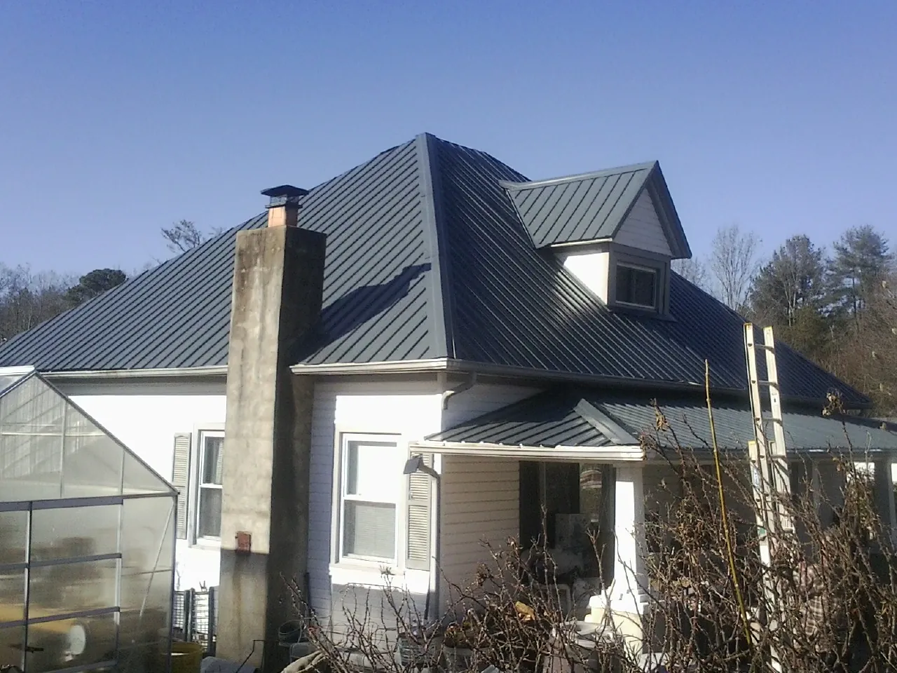 Dark blue standing seam metal roof on a white farmhouse with dormer — Slate & Tile Roof Repair by Roofing Brothers in Kindred