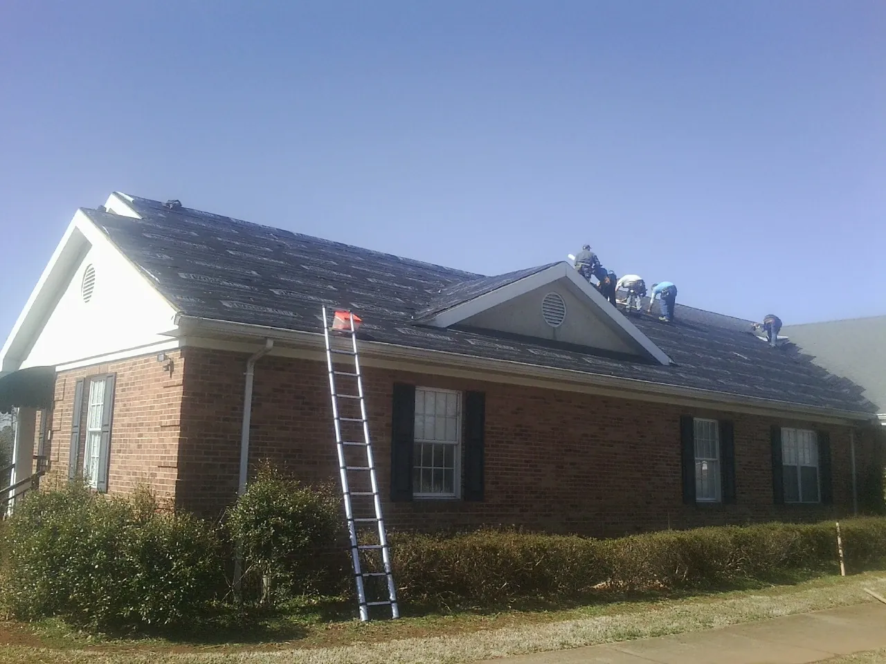 Crew tearing shingles off a brick ranch roof with a ladder set — Metal Roof Repair work by our crew in Kindred