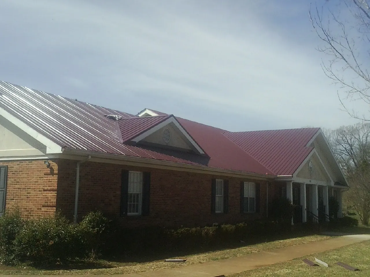 Red metal roof with gabled entries on a long brick building, from a Hail Damage Roof Repair job in Kindred