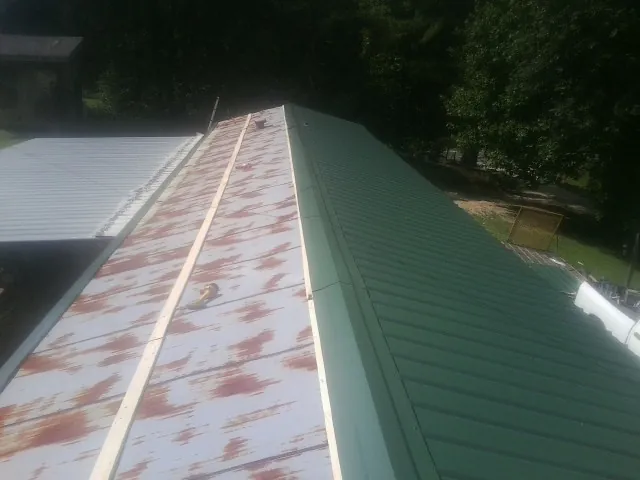 Old rusted panels beside newly installed green metal roofing — Wind Damage Roof Repair by Roofing Brothers in Kindred