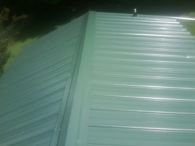 New green metal panels meeting at the ridge of a roof — Flat Roof Repair work by our crew in Kindred