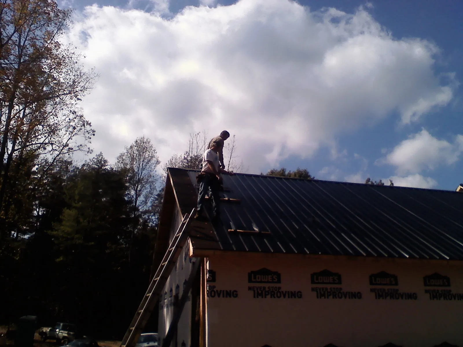 Roofer fastening dark metal panels high against a cloudy sky, from a Roof Inspection job in Kindred