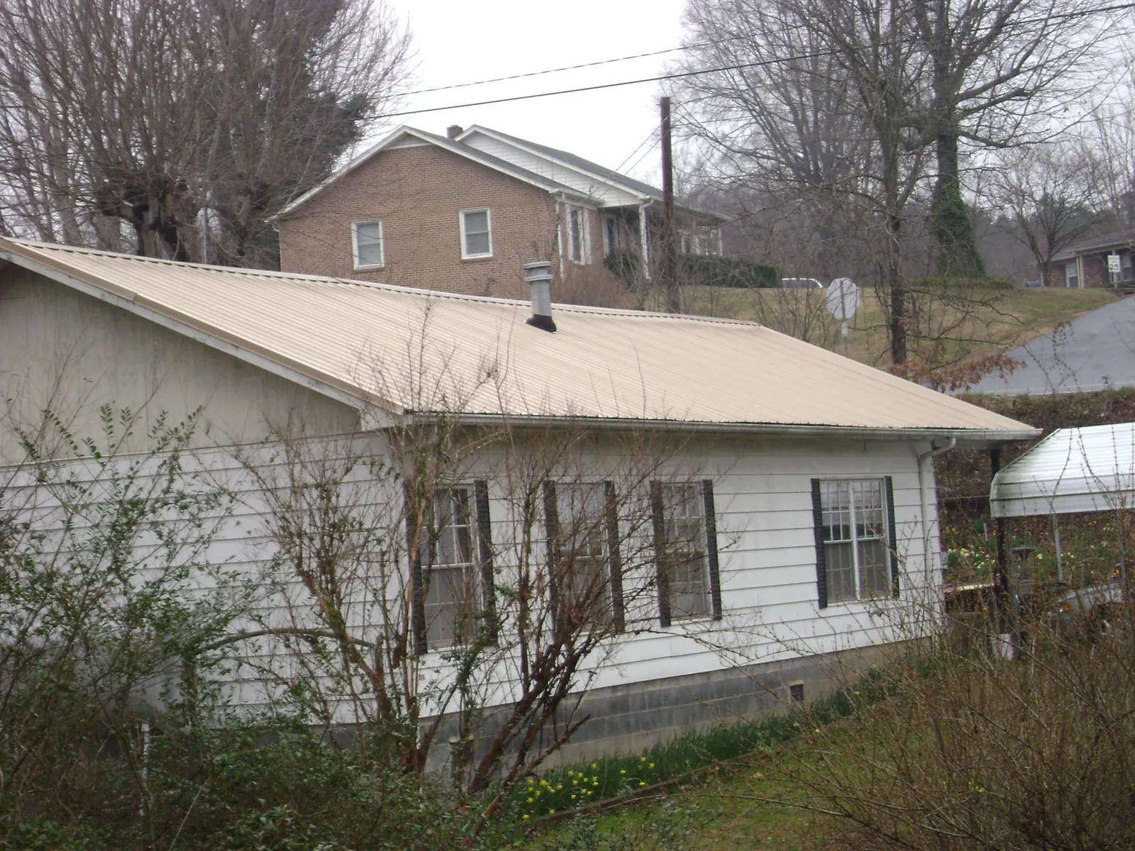 Tan metal roof on a white sided house set into a hillside — Commercial Roofing by Roofing Brothers in Kindred