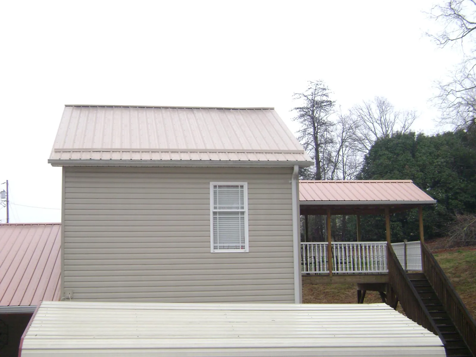 Tan metal roofs on a two story addition and attached porch, from a Roof Replacement job in Kindred